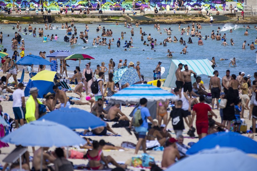 A large crowd of people gather to swim, walk, and play on a beach and in the nearby water.