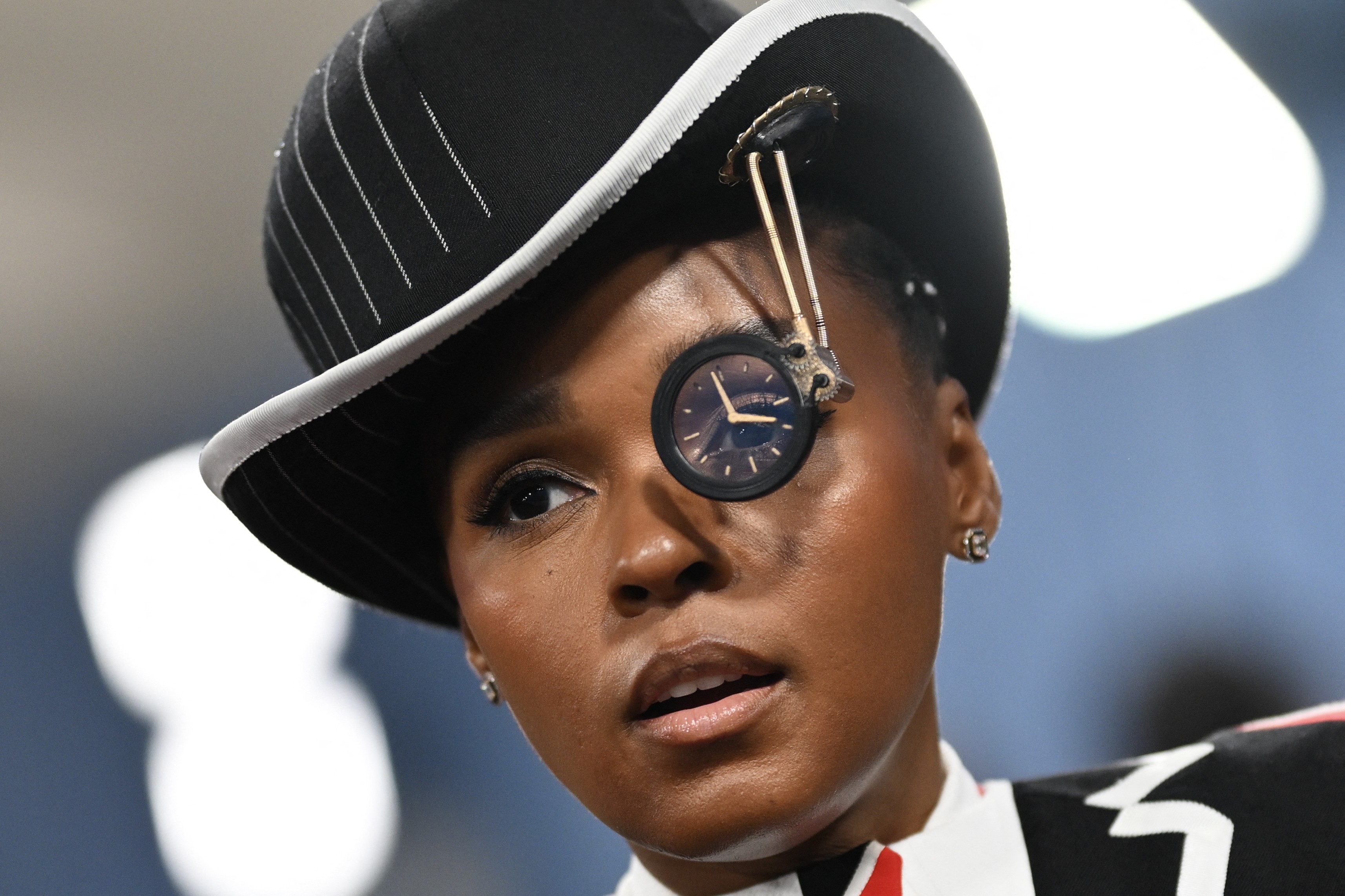 Janelle Monae wears a costume featuring a hat with an unusal eyepiece.