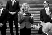 Representative Marjorie Taylor Greene smiles while holding a black face mask that reads "Stop the Steal."