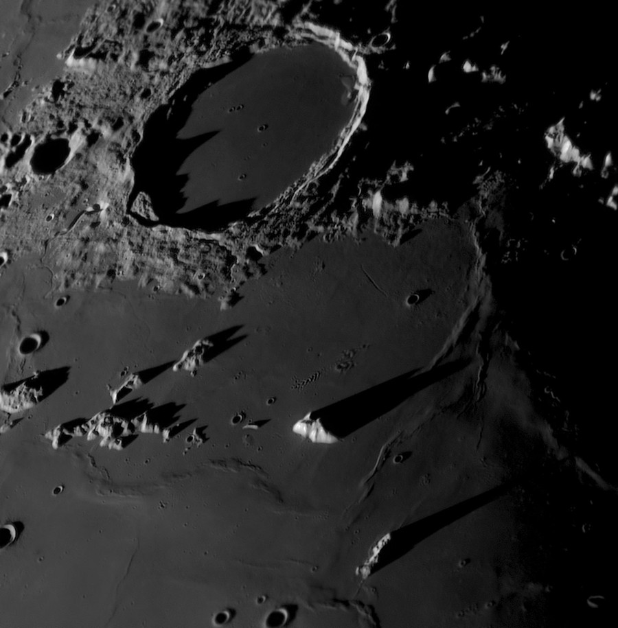 A view of the moon's surface, with many mountains and crater rims casting long shadows.