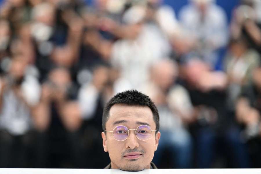 A person playfully poses for photographers, resting their chin on a tabletop, appearing to be only a head.