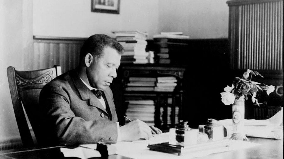 Booker T. Washington sits writing at his desk
