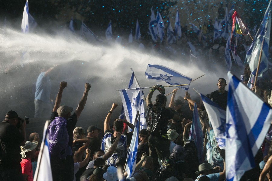 Protesters chant and wave Israeli flags as a spray of water is directed toward them.