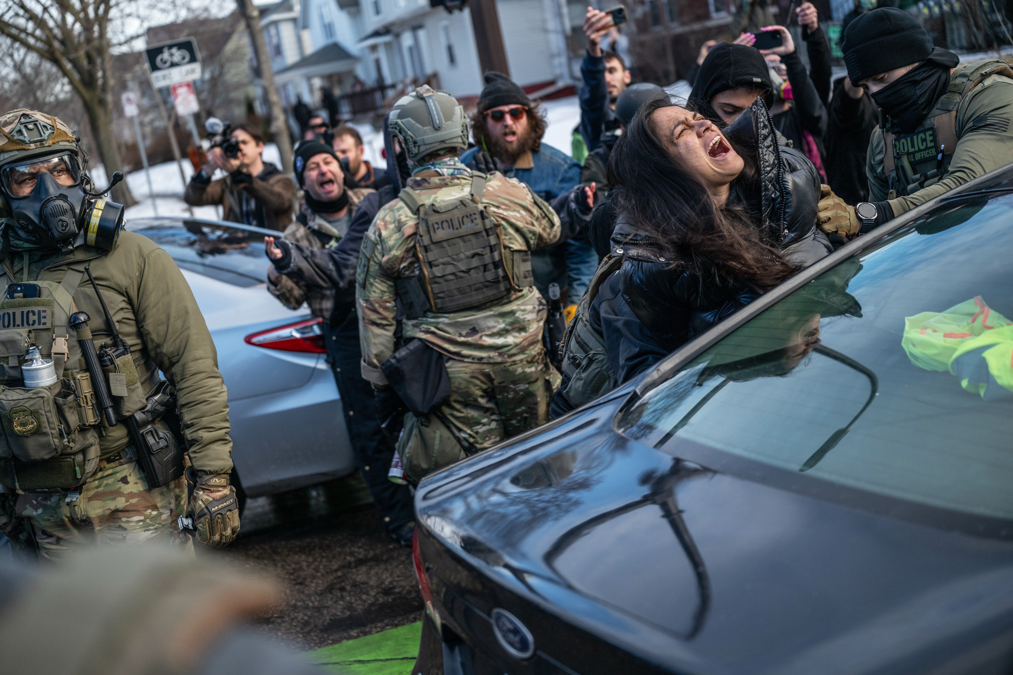 A woman cries out as she is removed from her car and arrested by federal agents, as onlookers shout in the background.