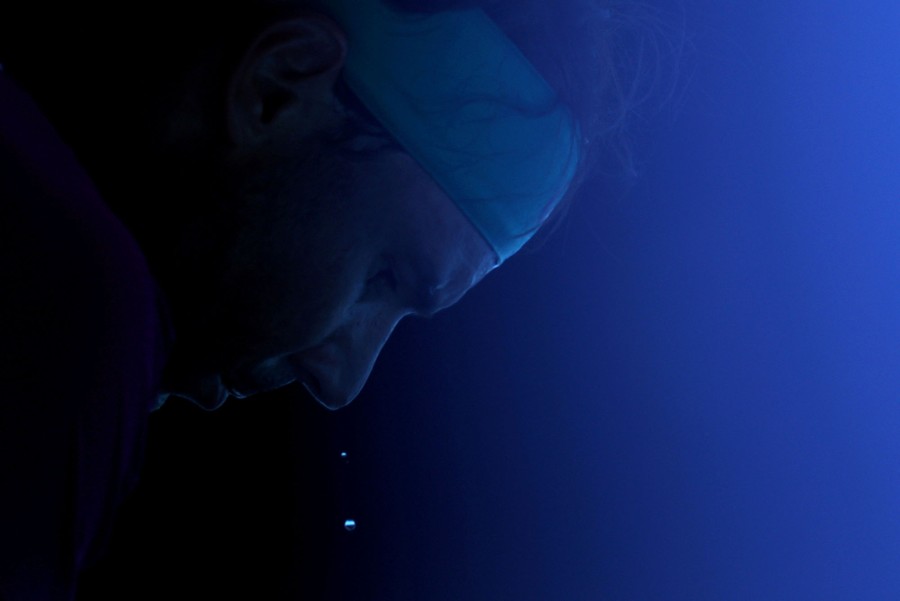 A close view of a tennis player who is leaning forward with sweat dripping off his face