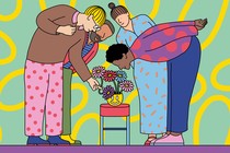 A group of people leaning over to admire a bouquet of flowers in a smiley vase