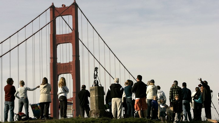 People gather on a hill in view of the Golden Gate Bridge