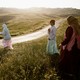 Girls walking along a road in Palestine, surrounded by rolling green hills, the sun beginning to set
