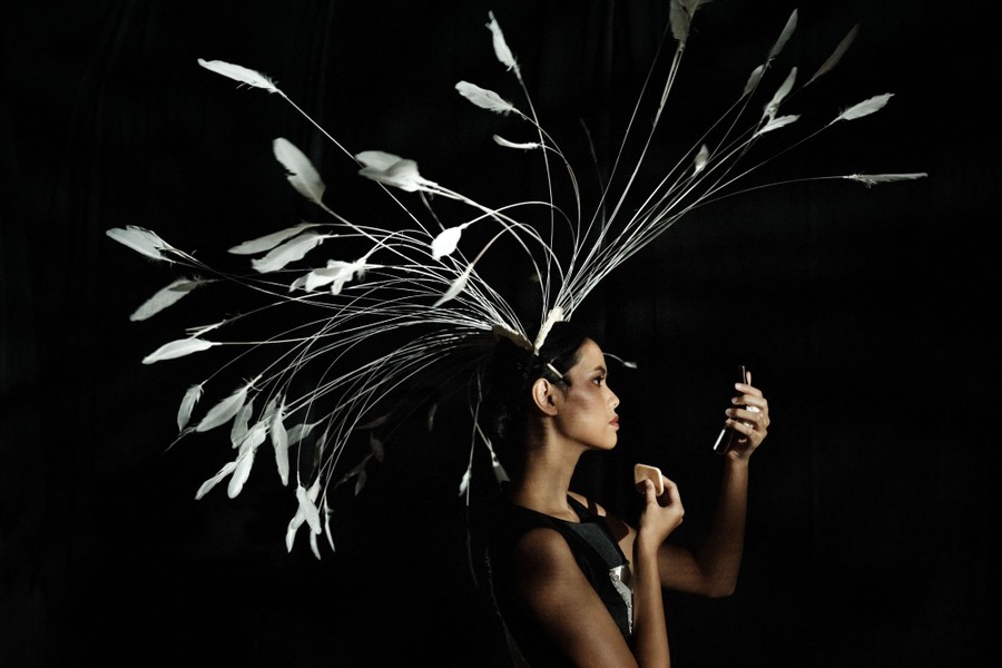 A model wears a head covering decorated with many long, white feathers.