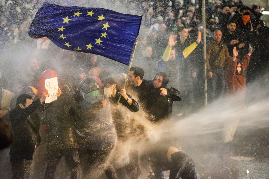 Protesters holding a European Union flag brace as they are sprayed by a water cannon.