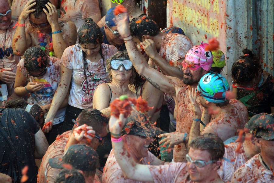 A crowd of people, covered in tomato pulp, play and throw tomato chunks.