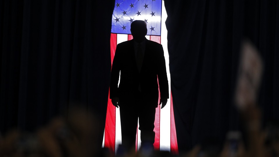 Trump is silhouetted against an American flag