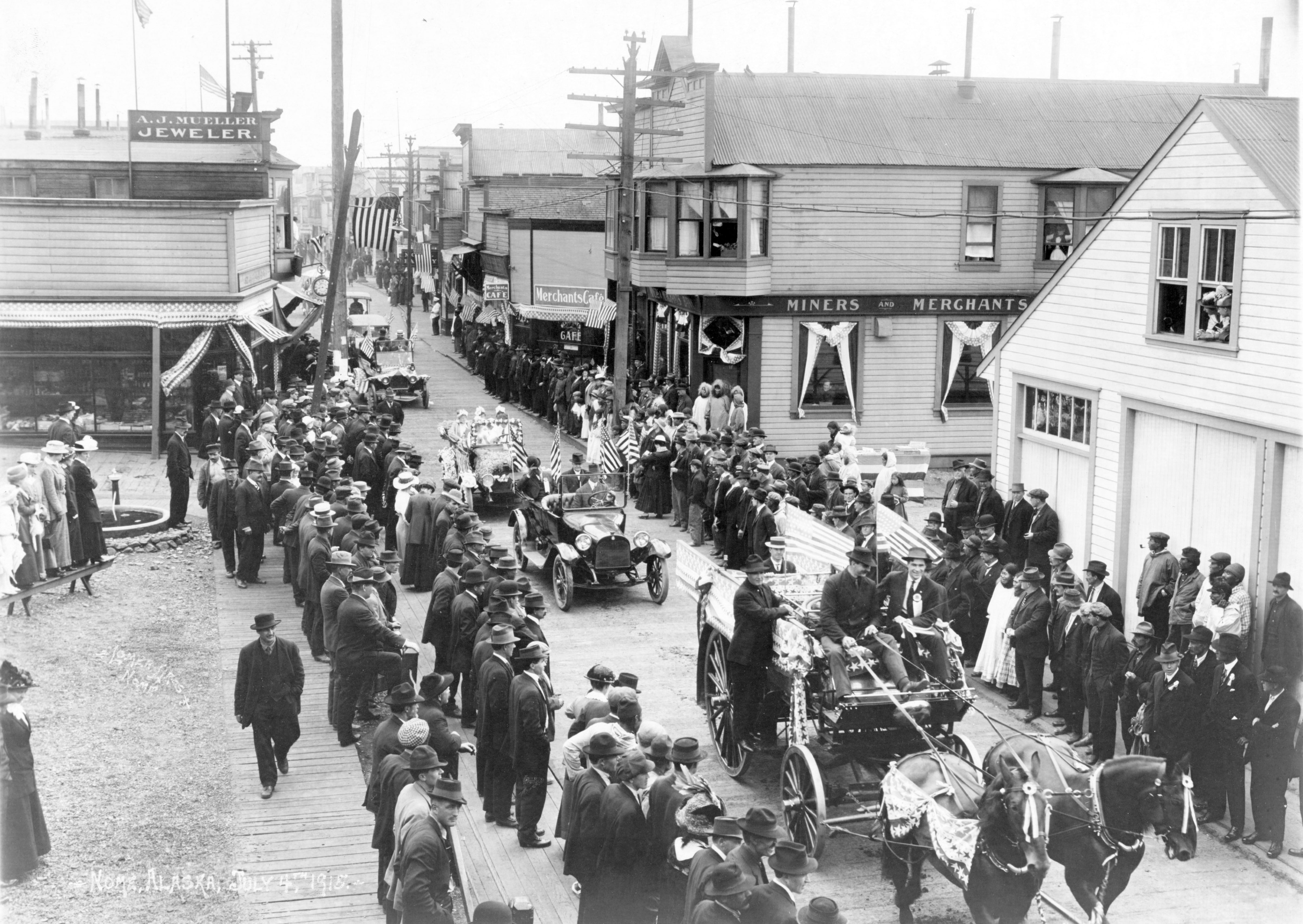 People stand on either side of a street, watching a Fourth of July parade in Nome, Alaska, in 1916.