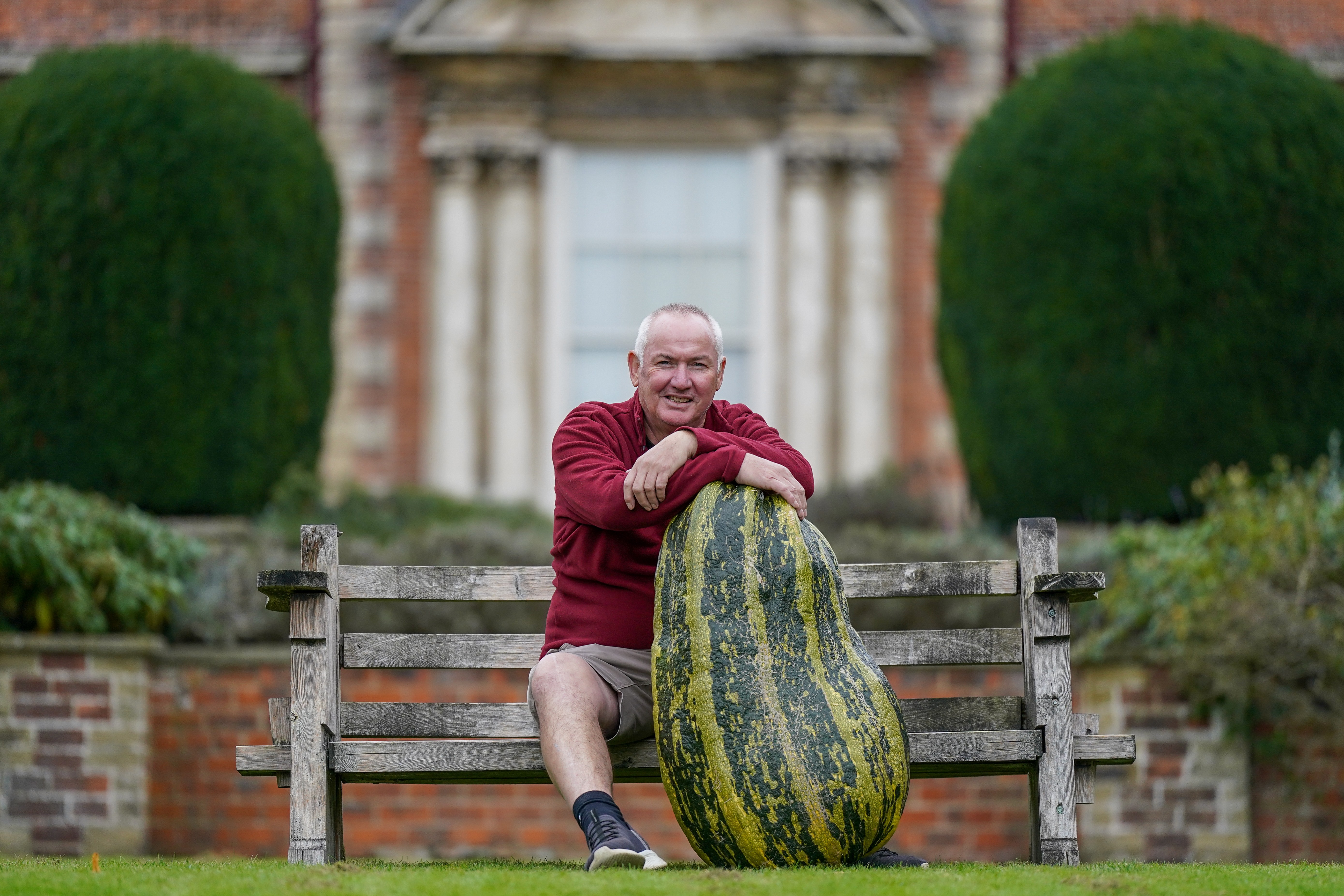 A man sits on a bench, proudly displaying his enormous squash.