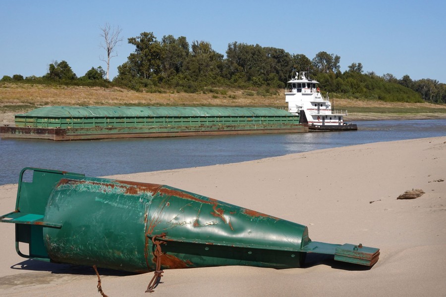 A tug pushes a barge past a grounded buoy on the Mississippi River.