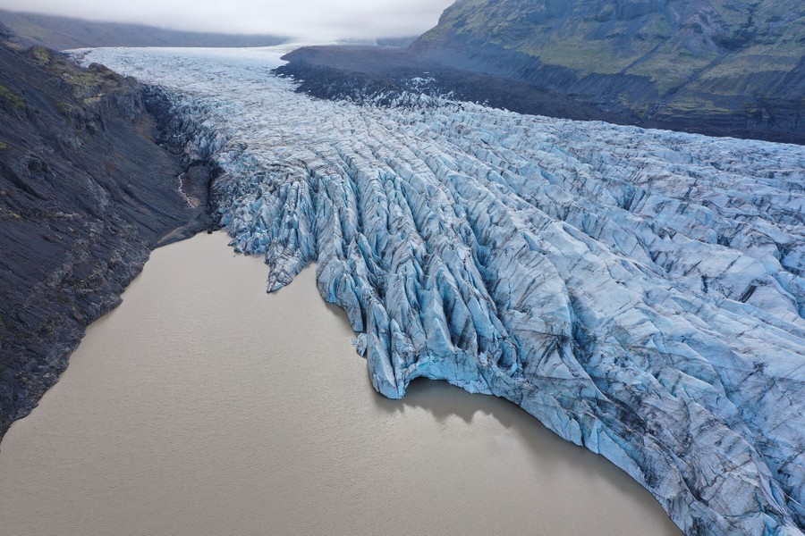 Deep crevasses can be seen at the end of a large glacier ending in a meltwater lake.