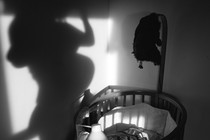 The shadow of a pregnant mother next to an empty crib