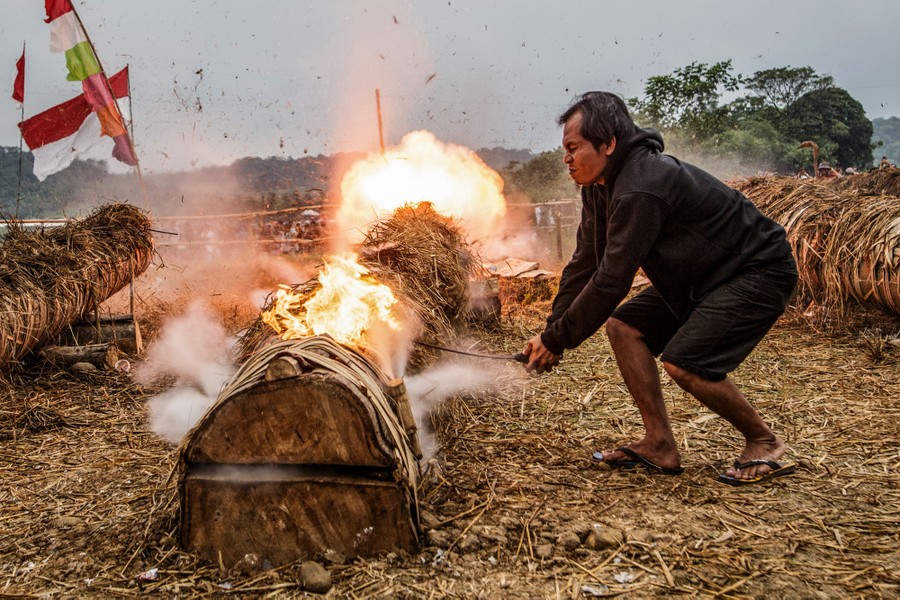 A person leans over with a small torch, igniting explosives inside a hollowed-out tree trunk.