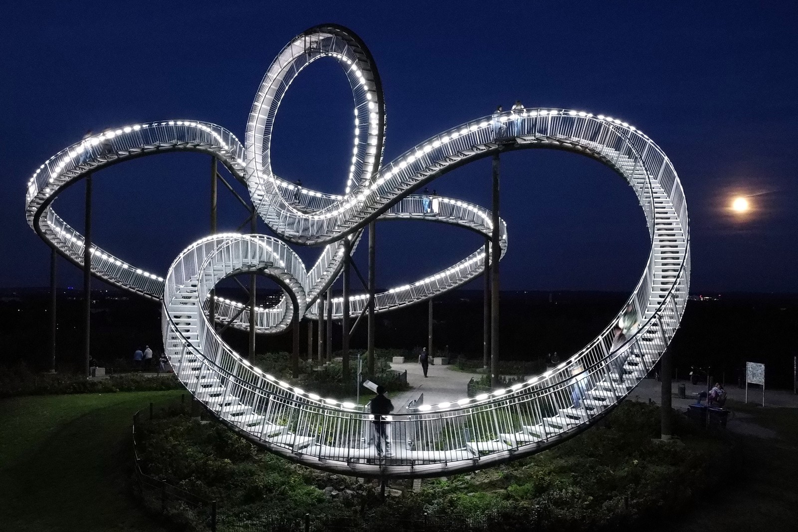 People visit a large outdoor sculpture—a long staircase that swoops and swirls like a rollercoaster.
