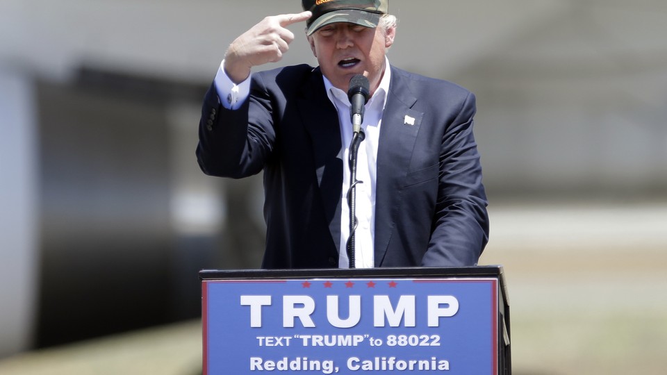 Republican presidential candidate Donald Trump gestures to a his camouflaged "Make America Great" hat at a campaign rally at the Redding Municipal Airport in Redding, Calif.