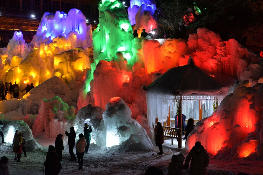 People walk among large frozen sculptures lit in many colors.