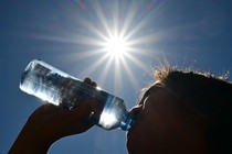 A photograph of a woman drinking from a water bottle, with a full afternoon sun blazing onto her.