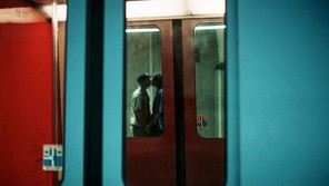 A photograph taken through subway train car doors, looking into another set of train car doors passing by, and a blurry couple holding hands and kissing inside that train