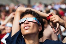 A person wearing eclipse glasses stares up at the sky.