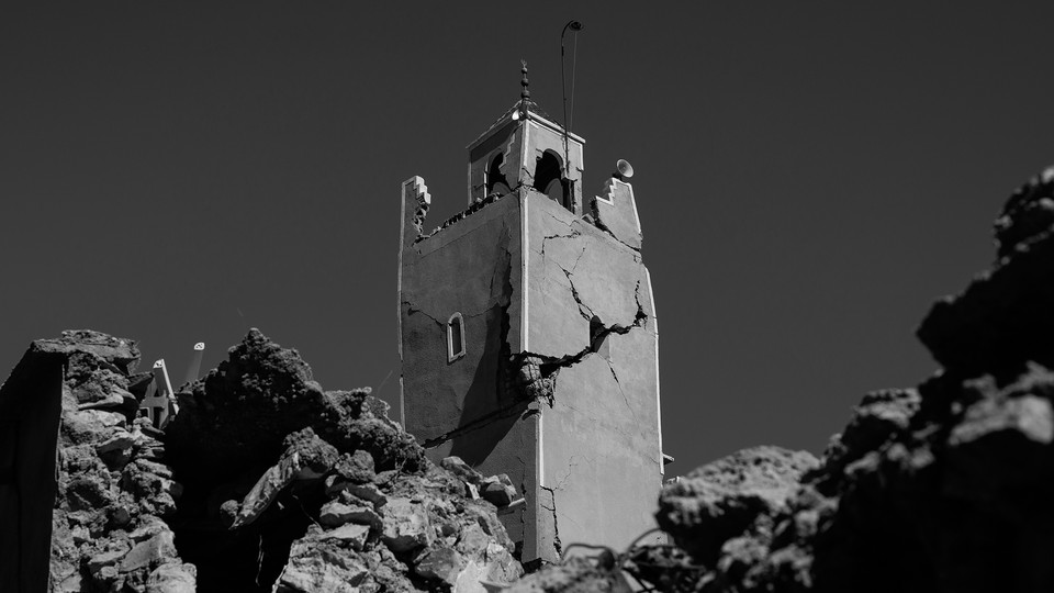 Black-and-white photograph of the cracked minaret of a mosque surrounded by rubble