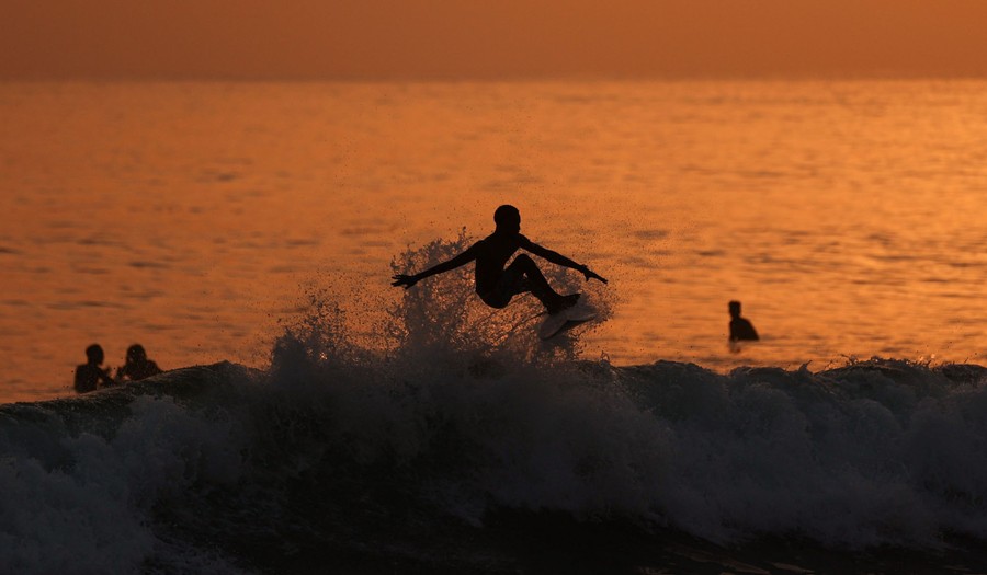 A surfer jumps above a small crashing wave.