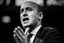 A black-and-white photo of Stephen Miller, with his hand in the foreground