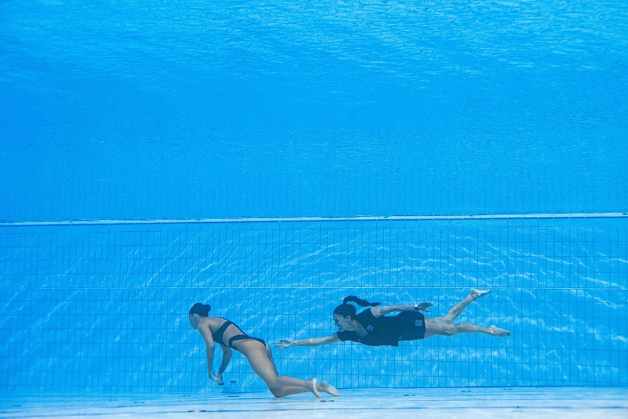 A woman swims underwater toward an unconscious swimmer at the bottom of a pool
