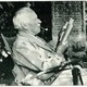 A black and white photograph of Jung in old age sitting in a yard, reading and holding a pipe in his mouth