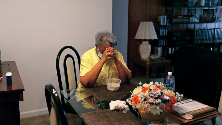 A woman sits at a table in her apartment, praying