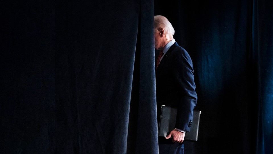 A photograph of Joe Biden walking behind a curtain