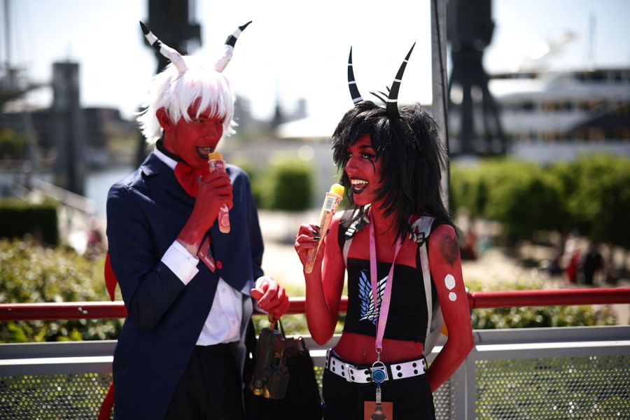 Two people dressed as devils enjoy frozen treats outside a convention center.