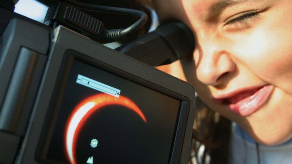 A boy watches an annular eclipse through a camera.