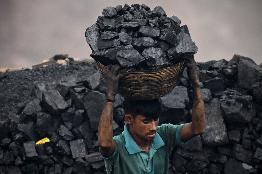 A person carries a large basket full of chunks of coal on top of their head.