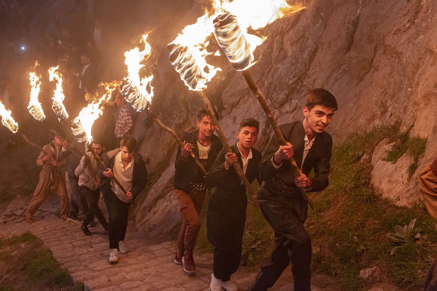 Several young men walk up a mountain path carrying large torches.