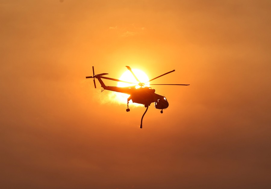 A firefighting helicopter passes in front of the sun.