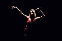 Celine Dion singing with a red leotard over black background