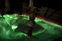 A view of an aurora above the Earth, green curtains of light scattered high above the clouds, seen from aboard the International Space Station.