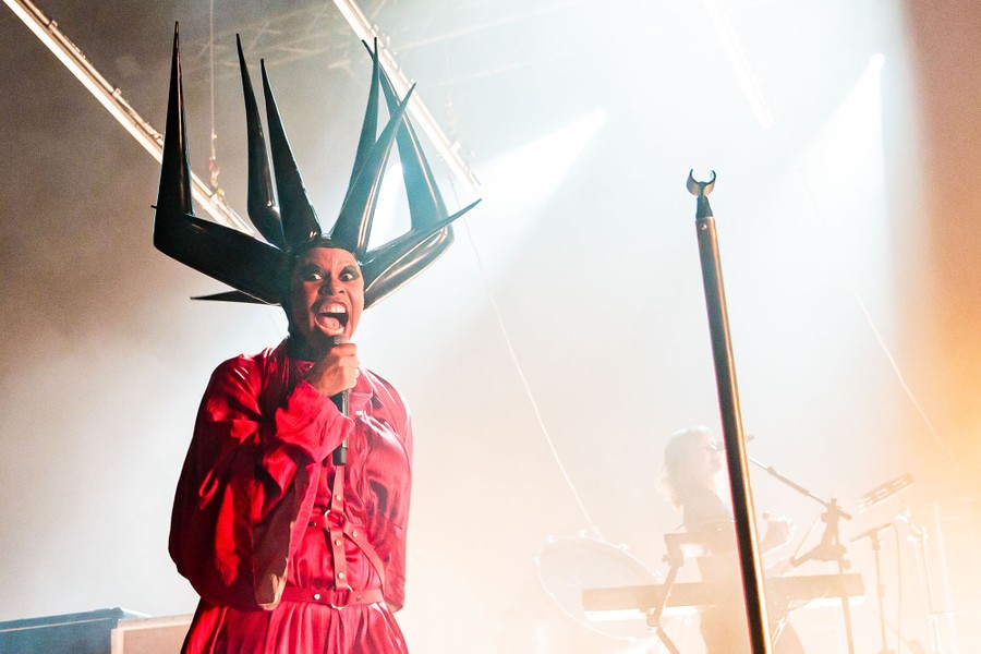A performer onstage wearing a large, spiky headpiece made of plastic
