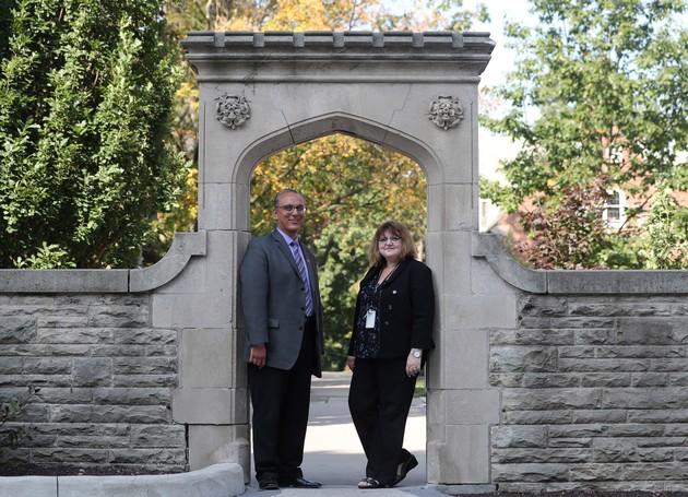 Two professors stand under an arch. 