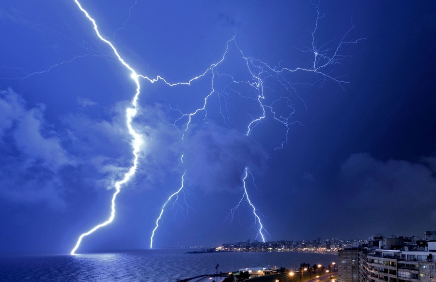 Lightning strikes during a thunderstorm at night, seen over a harbor.