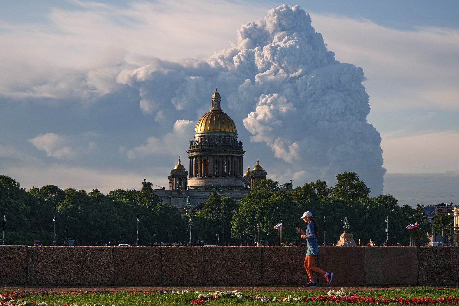 A person jogs in front of a cathedral, with a rising cloud of smoke in the background.