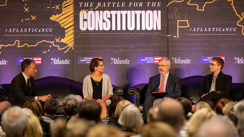 Four people sit on a stage in front of a sign that reads "The Battle for the Constitution"