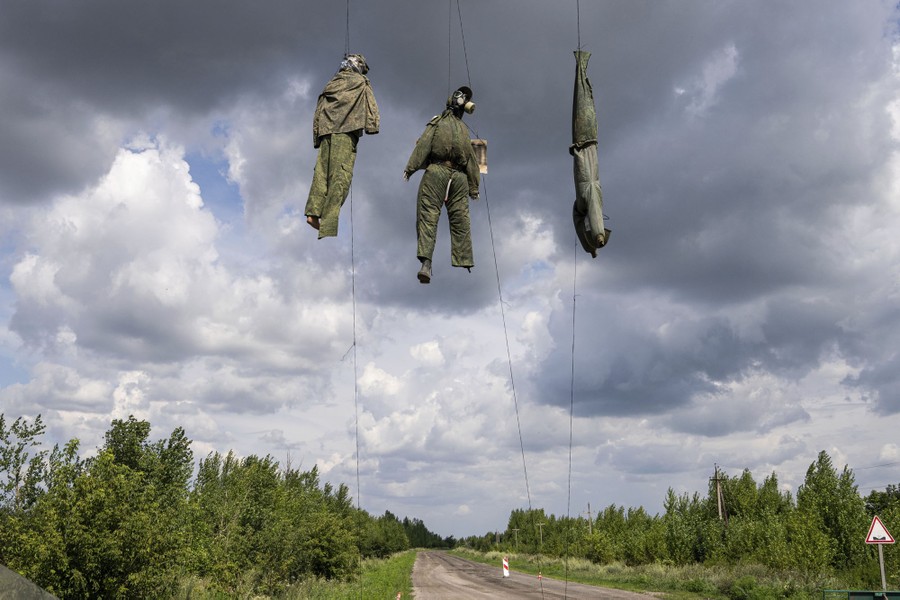 Three dummies made with military uniforms hang from rope above a road.