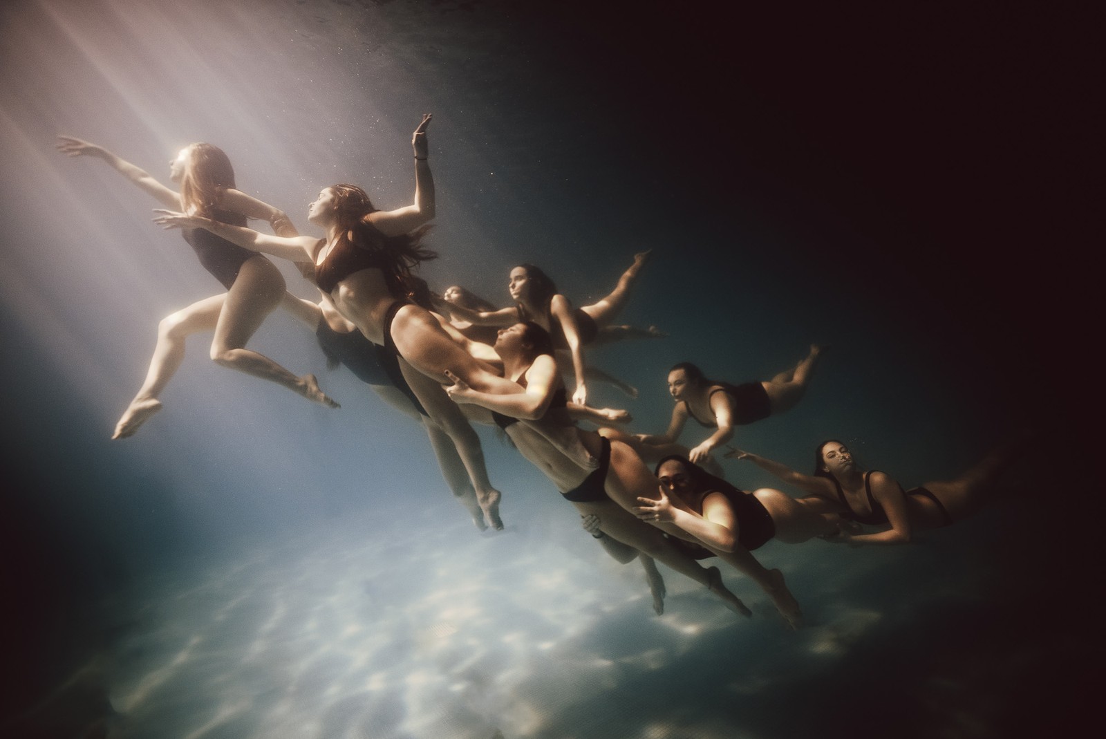 A group of synchronized swimmers pose in a cluster underwater, in a swimming pool.