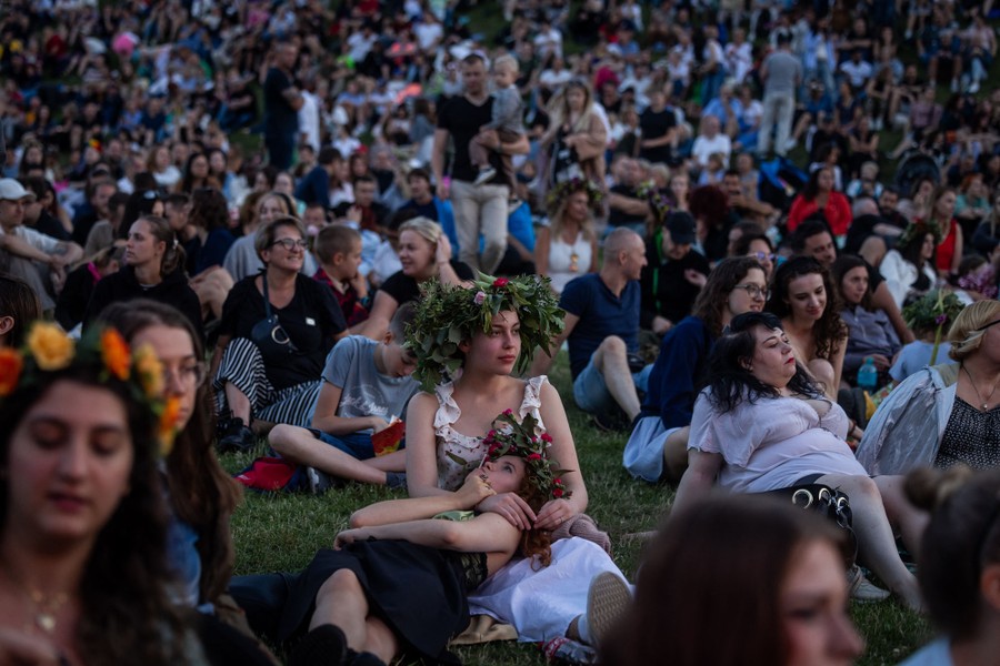 A crowd sits on grass, watching a concert.